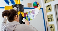 Eine Person bemalt ein großes, buntes Kunstobjekt in einem Atelier.